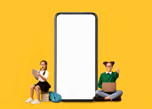 Little school girls showing white empty smartphone screen - Photo, image