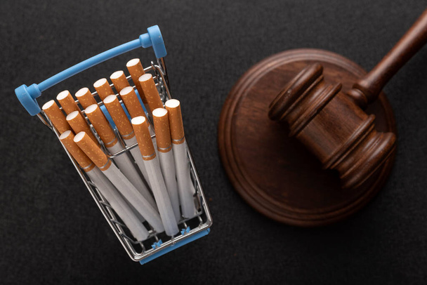Сигарети в кошику для покупок і судді забивають на чорному тлі. Заборона сигарет. Тютюнове право. Незаконний продаж сигарет
 - Фото, зображення