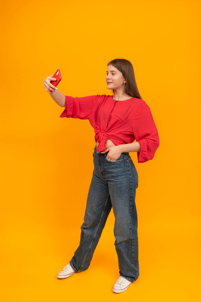 Full-leigh portrait of young girl with phone and takes selfie. Modern teenager. Portrait of girl on bright yellow background - Foto, immagini