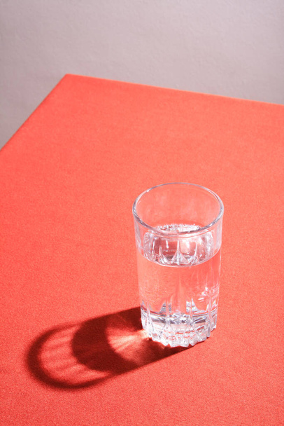 Szklanka wody z twardym cieniem na stole z czerwoną tkaniną. - Zdjęcie, obraz