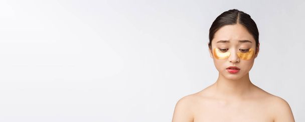 Asiatische Schönheit Teenager Frau pflegen ihre Haut mit goldenen Augenmasken Flecken unter den Augen mit Sorge. - Foto, Bild