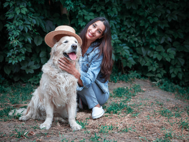 Portrait of yound happy woman playing with golden retriever labrador dog and straw hat - Photo, Image