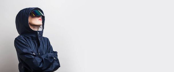 Giovane donna in occhiali di realtà virtuale, in giacca blu con le braccia incrociate su uno sfondo chiaro. Bandiera. - Foto, immagini