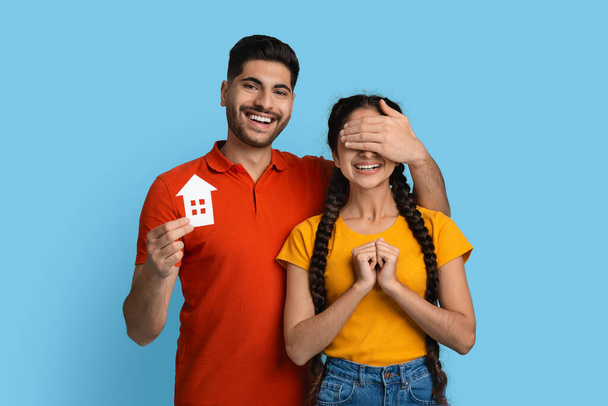 Happy arab guy holding paper house icon and covering girlfriends eyes - Foto, immagini