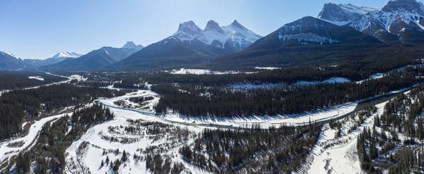 Bow River valley forest in winter. Snowcapped Canadian Rockies beautiful scenery. Aerial panorama view. Three Sisters ridge and Mount Lawrence Grassi mountain range. Canmore, Alberta, Canada. - Photo, Image