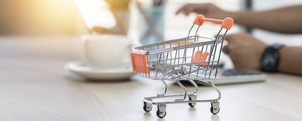 shopping cart on table with hand of people on laptop background  - Photo, Image
