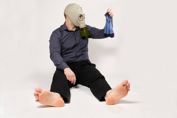 A barefoot man in a gas mask holds dirty smelly socks. The problem of unpleasant foot odor in men - Fotografie, Obrázek