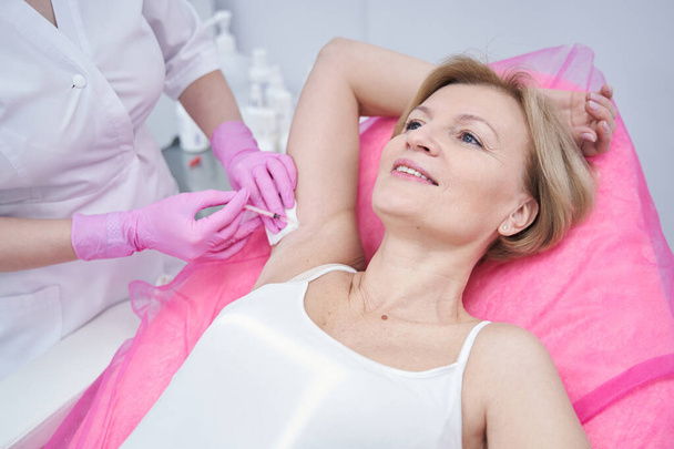 Woman receiving underarm injection in beauty salon - Foto, imagen