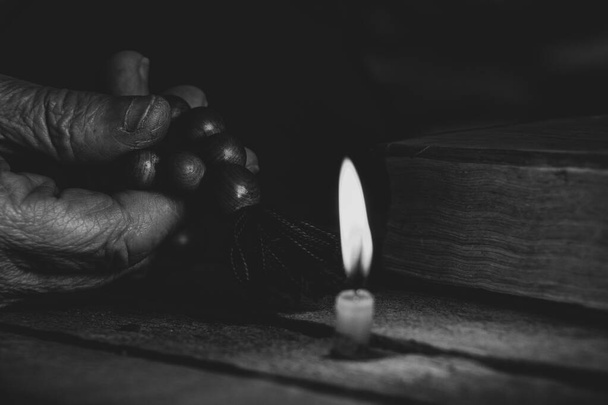 Nainen, jolla on puinen rukousnauha ja raamattu oksensi kynttilöitä pimeässä, nainen rukoilee, rukoilee, usko ja uskonto, temppeli - Valokuva, kuva