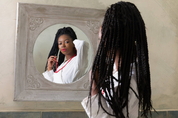 Pretty young african american woman doing her morning routine in front of the bathroom mirror - Fotó, kép
