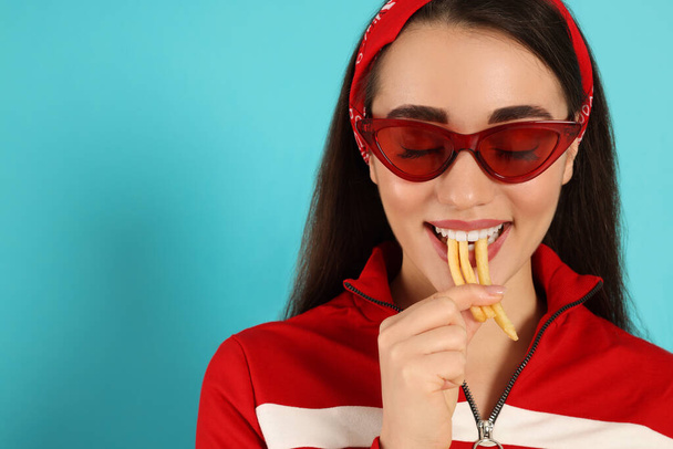 Beautiful young woman eating French fries on light blue background. Space for text - Fotografie, Obrázek