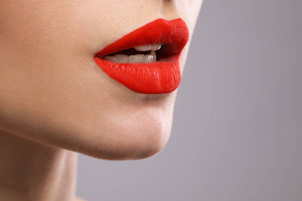 Young woman with beautiful red lips on grey background, closeup. Space for text - 写真・画像