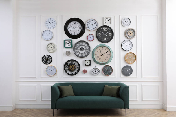 Collection of different clocks and comfortable sofa in stylish room. Interior design - Fotografie, Obrázek