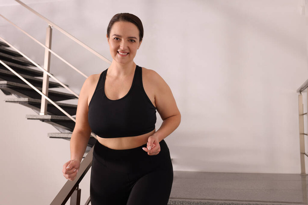 Happy overweight woman in sportswear on stairs indoors, space for text - Foto, Imagem