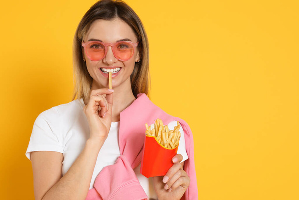 Young woman eating French fries on yellow background, space for text - Фото, зображення