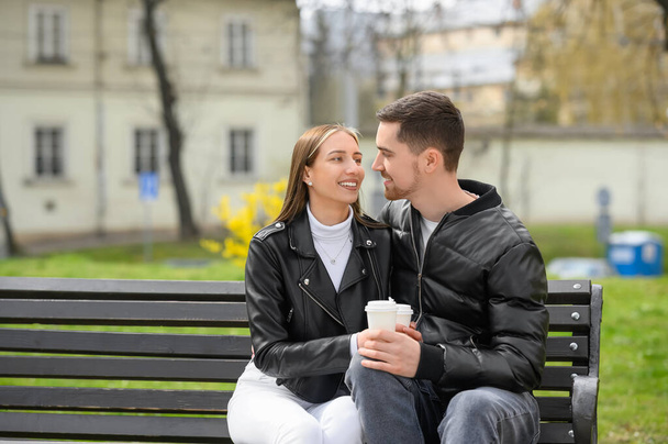 Lovely young couple with cups of coffee on bench outdoors. Romantic date - Fotó, kép