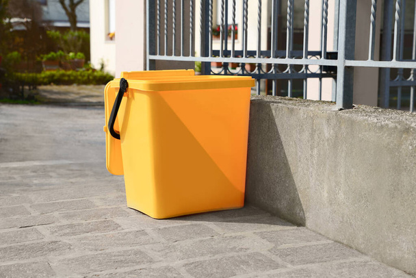 Yellow trash bin near fence outdoors on sunny day - Foto, afbeelding
