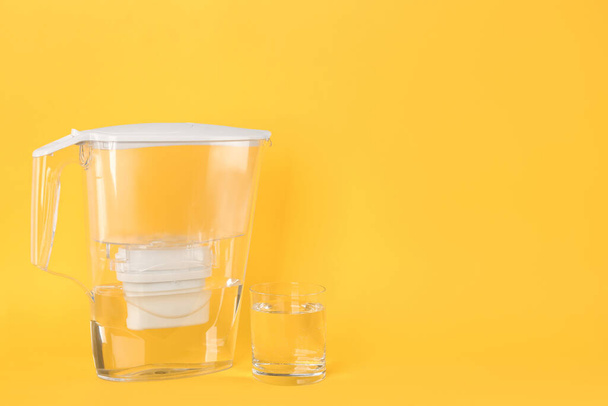 Filter jug and glass with purified water on yellow background. Space for text - 写真・画像