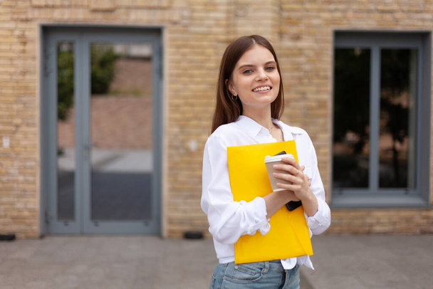 First day at work. Cheerful girl with a folder, portrait of a student. - Foto, afbeelding