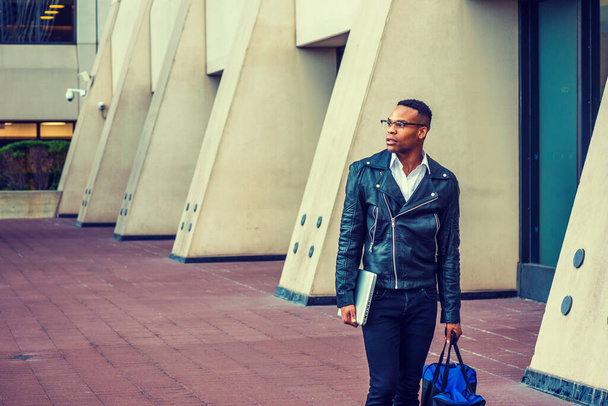 Man Urban Casual Fashion. Nošení černé kožené bundy, džíny, kožené boty, brýle, držení notebooku, nošení tašky, Afroameričtí vysokoškoláci procházející se po ulici v New Yorku. - Fotografie, Obrázek
