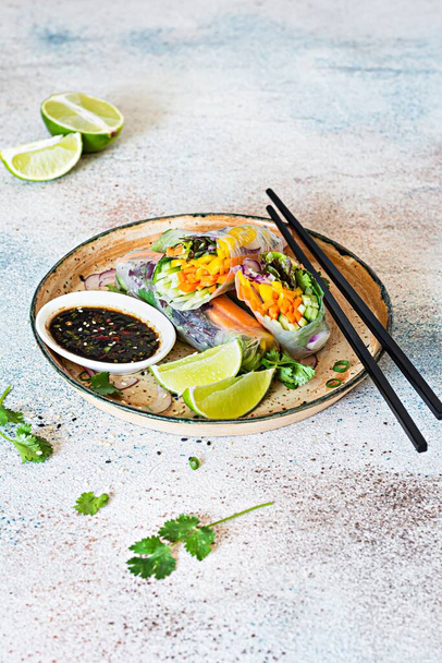 Frische asiatische Vorspeise Frühlingsrollen (Nem) aus Reispapier und rohem Gemüse und Kräutern mit scharfer Sauce auf hellblauem Hintergrund. Vietnamesisches Essen - Foto, Bild