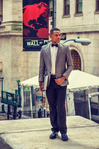 African American Businessman working in New York, wearing gray blazer, bow tie, black pants, leather shoes, holding laptop computer, standing on Wall Street, thinking. Filtered effect. - Zdjęcie, obraz