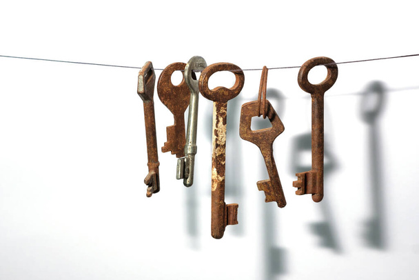 A different old retro rusty keys from different locks hanging on string with a drop shadow on a white wall - Фото, зображення