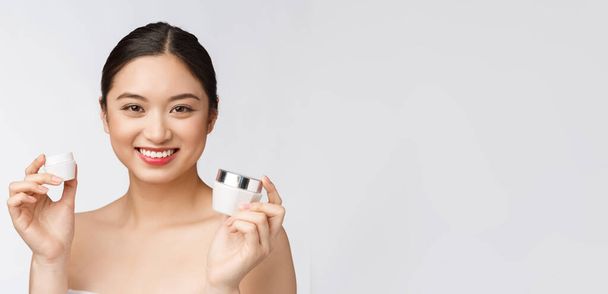 schöne junge Frau auf weißem isolierten Hintergrund hält kosmetische Gesichtscreme, asiatische - Foto, Bild