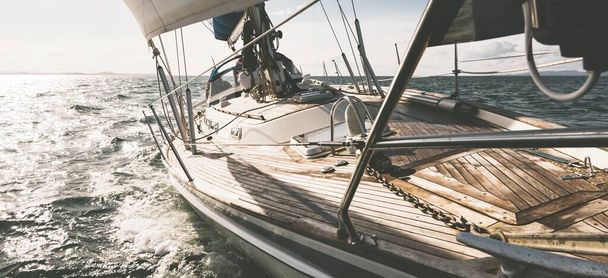 Sloop felszerelte a modern jachtot fából készült teak fedélzettel, ami végigszáguldott a hullámokon. Kilátás a fedélzetről az orrra. A víz közelről fröcsköl. Islay-sziget, Belső-Hebridák, Skócia, Egyesült Királyság. Sport és rekreáció - Fotó, kép