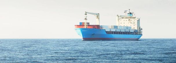 Groot blauw vrachtcontainerschip met een kraan die in open zee vaart. Verenigde Staten. Goederenvervoer, nautisch schip, wereldwijde communicatie, logistiek, scheepvaart, levering, industrie, handel, economie - Foto, afbeelding