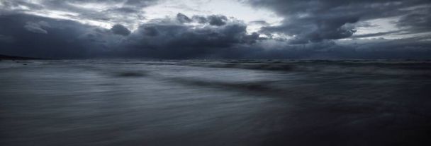 Temná bouřková obloha nad Baltským mořem, vlny a vodní šplouchání. Dramatická oblačnost. Příroda, životní prostředí, nestálé počasí, změna klimatu. Atmosférická scenérie. Panoramatický výhled, dlouhé vystavení - Fotografie, Obrázek