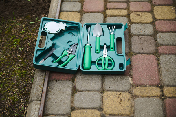Vue de dessus de la valise avec des outils de jardinage pour le jardinage et passe-temps agricole sur un trottoir à côté d'un potager - Photo, image