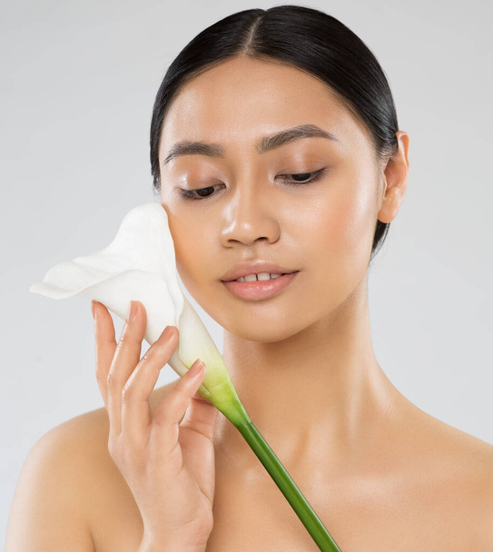 Skin Care. Natural Beauty Woman holding White Calla Lilly Flower. Asian Model with Fresh Clean Skin Make up looking down. Facial Eco Treatment and Facelift Spa Massage Cosmetology - Фото, изображение