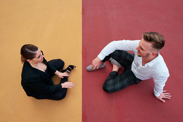 Top view of a businesswoman and a businessman talking while sitting on the ground outdoors. - 写真・画像