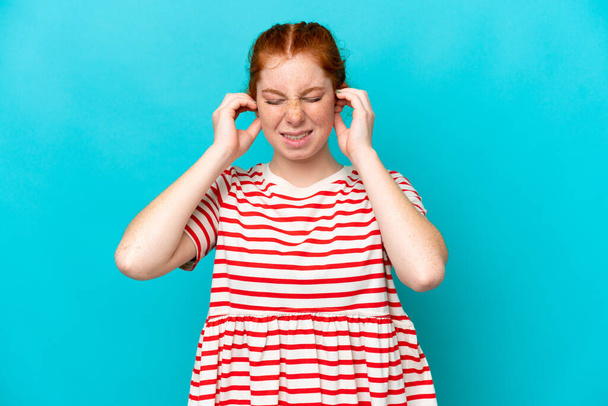 jonge roodachtige vrouw geïsoleerd op blauwe achtergrond gefrustreerd en het bedekken van oren - Foto, afbeelding