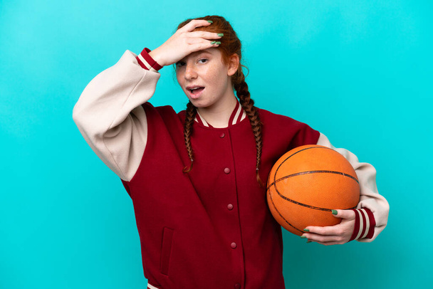Young reddish woman playing basketball isolated on blue background doing surprise gesture while looking to the side - Фото, зображення