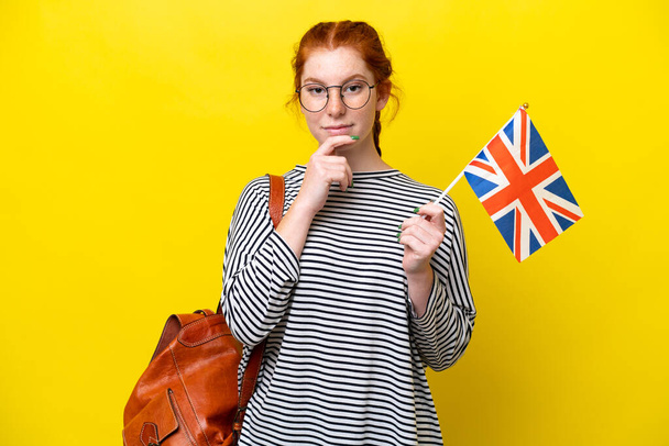 Young hispanic woman holding an United Kingdom flag isolated on yellow background thinking - Fotó, kép