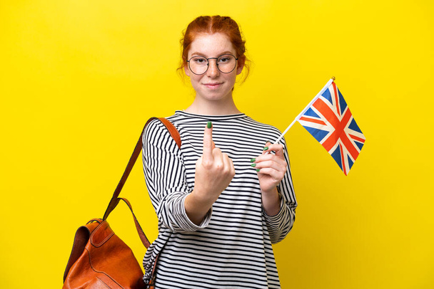 Young hispanic woman holding an United Kingdom flag isolated on yellow background doing coming gesture - Foto, Bild