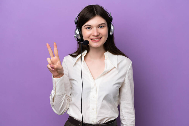 Telemarketer Russian woman working with a headset isolated on purple background smiling and showing victory sign - Foto, imagen