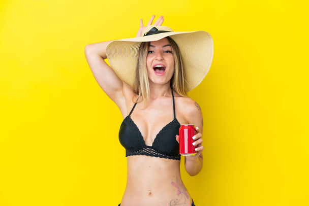 Young Romanian woman isolated on yellow background in swimsuit and holding a cocktail - Photo, Image