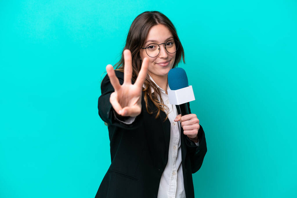Young TV presenter woman isolated on blue background happy and counting three with fingers - Fotografie, Obrázek