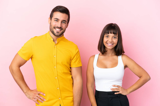 Young couple isolated on pink background posing with arms at hip and smiling - Photo, Image