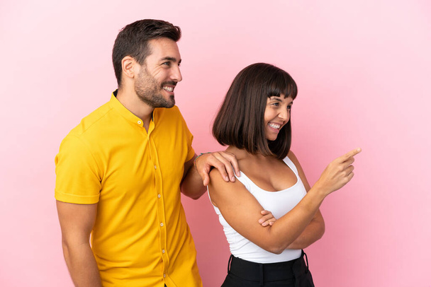 Junges Paar isoliert auf rosa Hintergrund zeigt auf die Seite, um ein Produkt zu präsentieren - Foto, Bild