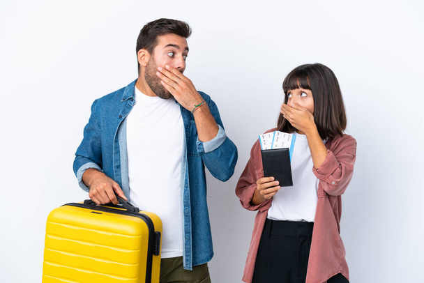 Молодая пара путешественников с чемоданом и паспортом на белом фоне, закрывая рот руками за то, что сказала что-то неуместное. - Фото, изображение