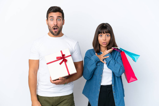 Young couple holding shopping bags and present isolated on white background with surprise and shocked facial expression - Fotoğraf, Görsel