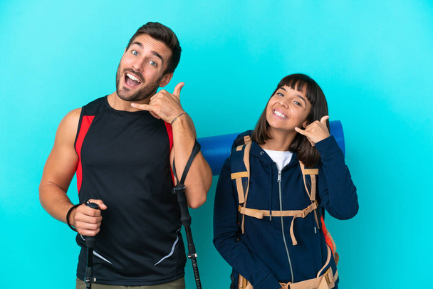 Young mountaineer couple with a big backpack isolated on blue background making phone gesture. Call me back sign - Photo, Image