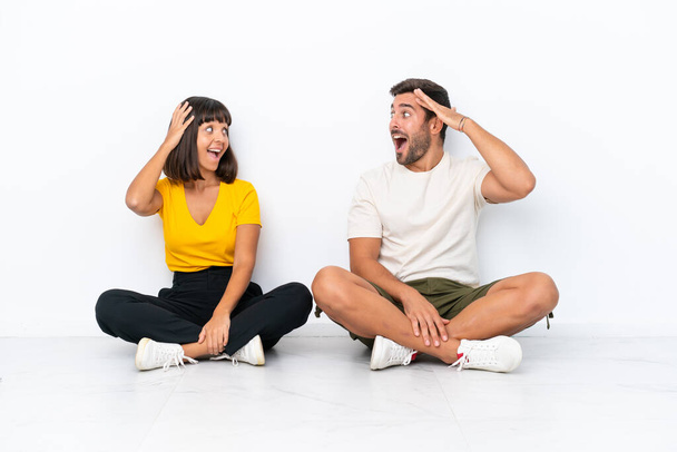 Young couple sitting on the floor isolated on white background with surprise and shocked facial expression - Photo, image