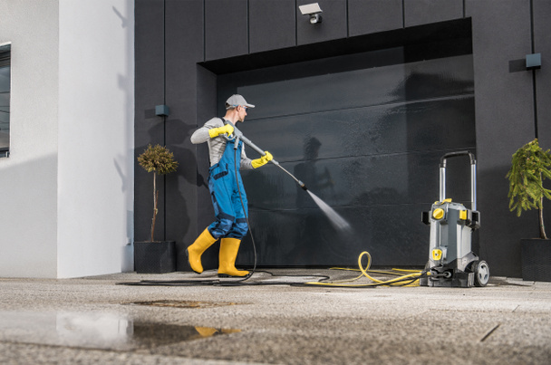 Kaukasische Männer waschen sein Garagentor mit Hochdruckreiniger. Tor und Auffahrt sauber halten.  - Foto, Bild