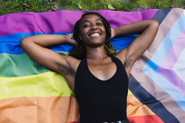 Black girl lying on LGTBQ flag rests after pride day. - Фото, изображение