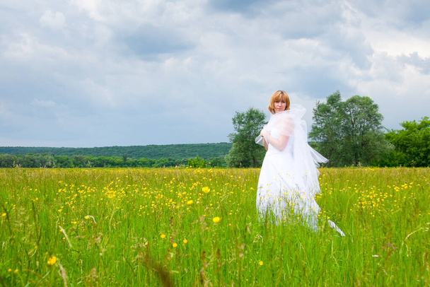 svatební den, krása, příroda. uprostřed pole je úžasná žena v bílých šatech nevěsty, točí se kolem sebe a flitry svítí ve světle slunce - Fotografie, Obrázek